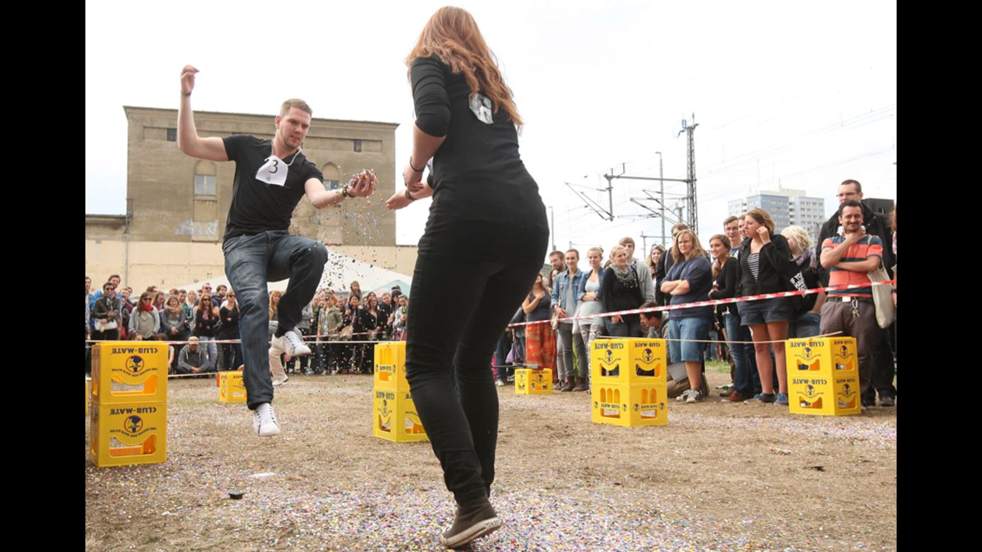 A man jumps over sticks that are laid across empty Club Mate crates to pass confetti to another participant. 