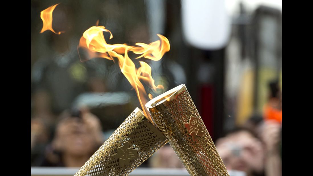 Torchbearers "kiss" their torches to pass the Olympic flame during the London 2012 torch relay through the Borough of Tower Hamlets in London on Saturday, July 21.