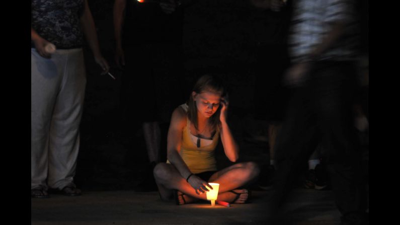 A woman holds a lit candle at a makeshift memorial.