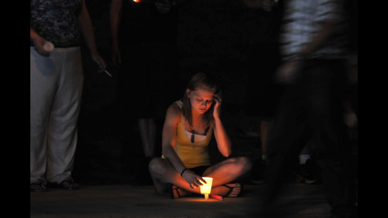A woman holds a lit candle at a makeshift memorial.