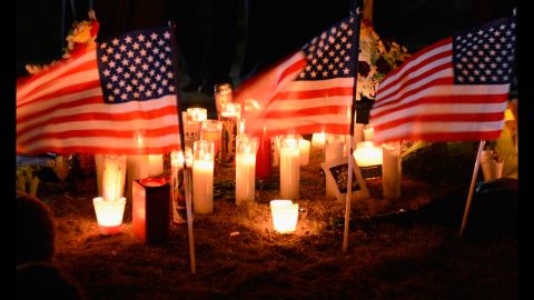 Flags, flowers and candles make up a memorial site.