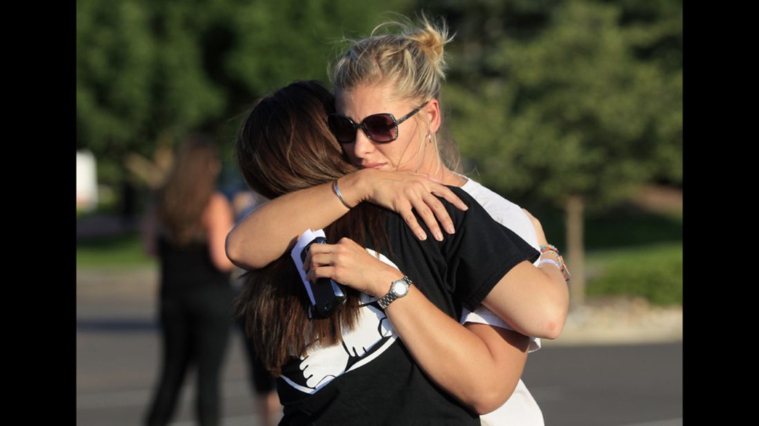 People embrace before a vigil for victims behind the theater where a gunman opened fire on moviegoers.