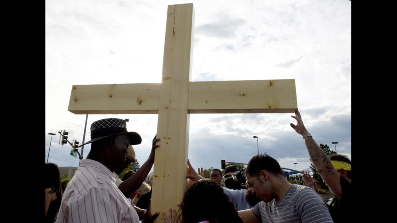 People pray at a cross erected at the makeshift memorial across the street from the Century 16 theater on Saturday.