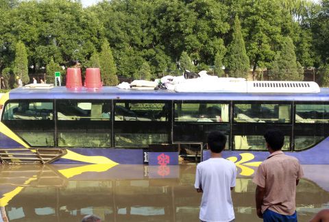 Two men watch as emergency services personnel try to retrieve a damaged bus which was submerged in a flooded carpark after a storm hit Beijing, July 22, 2012.