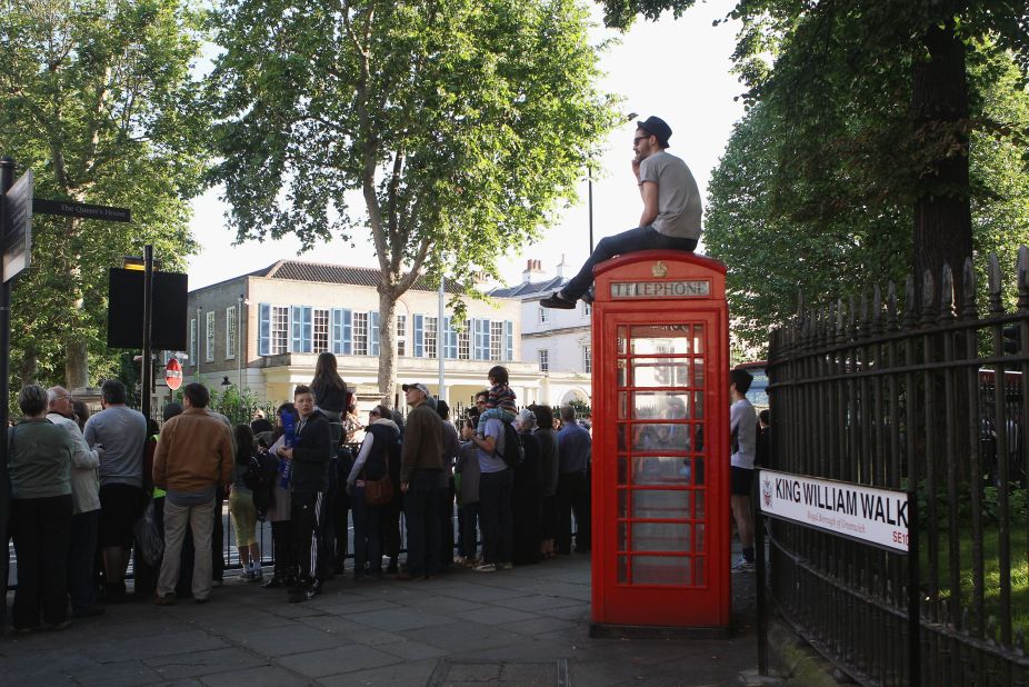 A spectator sits atop a phone booth as people gather to watch the Olympic torch pass through Greenwich in London on Saturday, July 21.