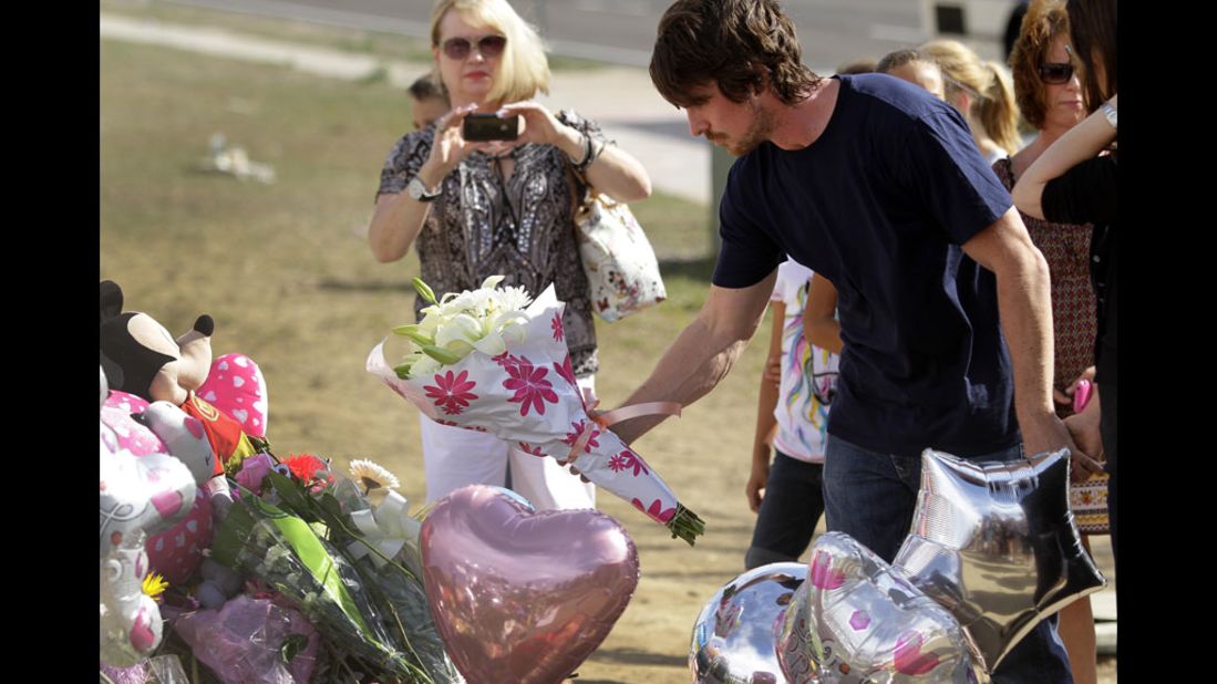 Bale places flowers at the memorial while other mourners look on.