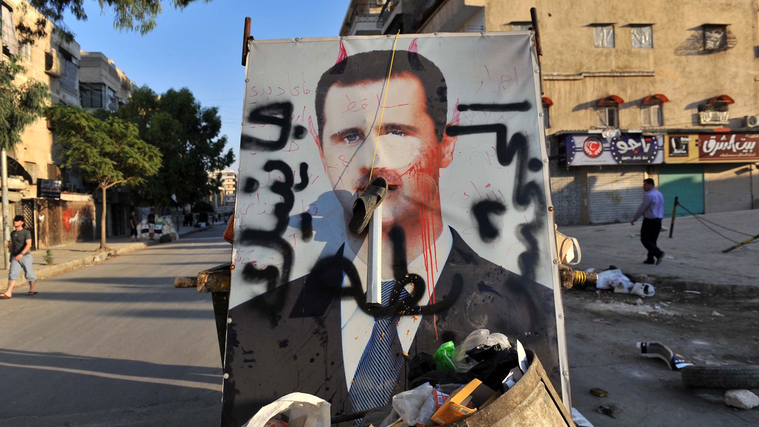 A vandalized poster of Syrian President Bashar al-Assad lies in a trash container in the northern city of Aleppo on Tuesday.