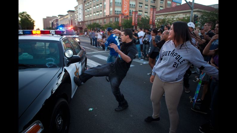 A man kicks a passing police car during a protest against Diaz's shooting.