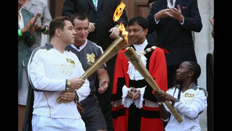 Torchbearer Rhyania Blackett-codrington, right, passes on the Olympic flame to comedian David Walliams, left, before setting off from Islington Town Hall July 26.