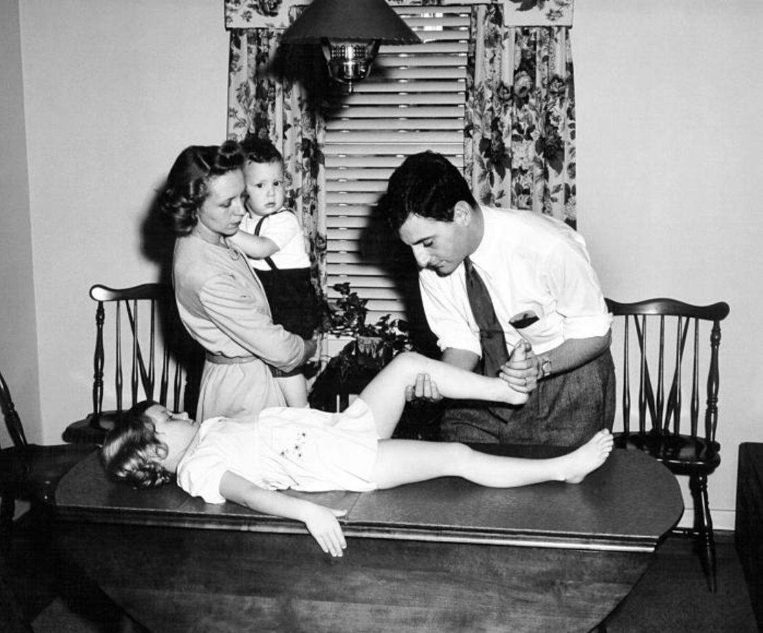 A public health officer evaluates the muscles of a young patient to test for polio.