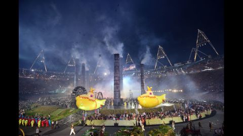 Inflatable yellow submarines float above artists during The Age of Industry scene.