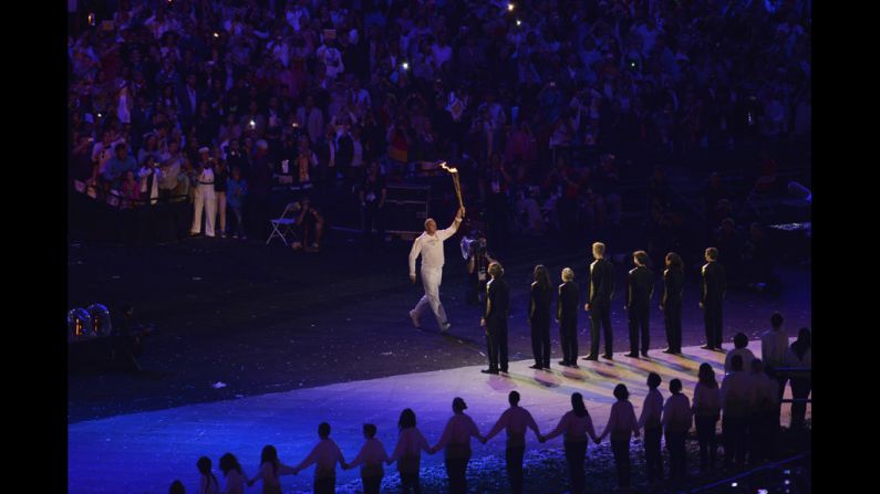 Five-time Olympic rowing gold medalist Steve Redgrave of Britain carries the torch during the opening ceremony and then hands it off to a group of young athletes.