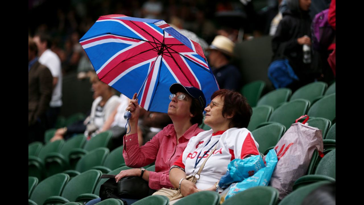 Fans at Wimbledon's Centre Court take shelter from a downpour under a Union Jack umbrella during a rain delay.