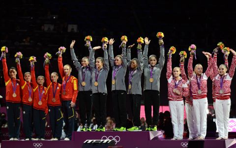Gold winners Team USA, center, silver winners Team Russia, right, and bronze winners Team Romania celebrate on the podium of the women's team competition of the gymnastics event.