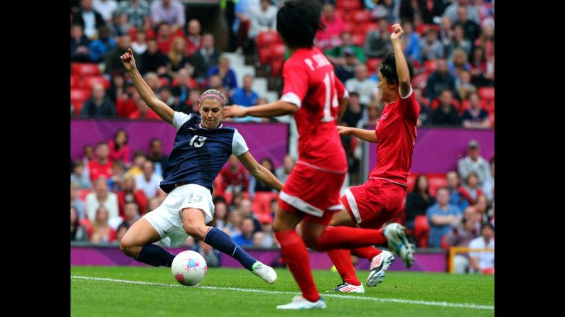 Alex Morgan of the United States strikes the ball while Kim Myong Gum and Pong Son Hwa of North Korea attempt to deflect during the women's soccer first-round match.