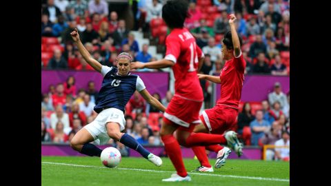 Alex Morgan of the United States strikes the ball while Kim Myong Gum and Pong Son Hwa of North Korea attempt to deflect during the women's soccer first-round match.