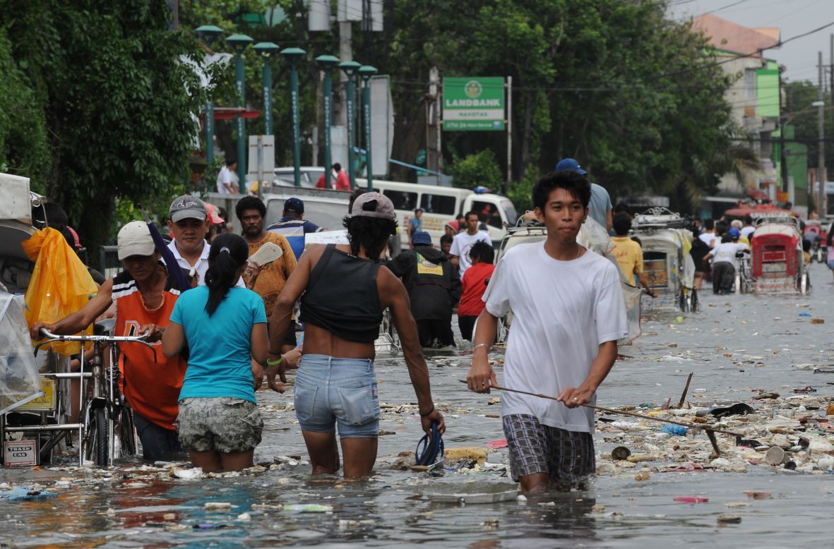 Residents wade through a flooded street filled with trash in Navotas.