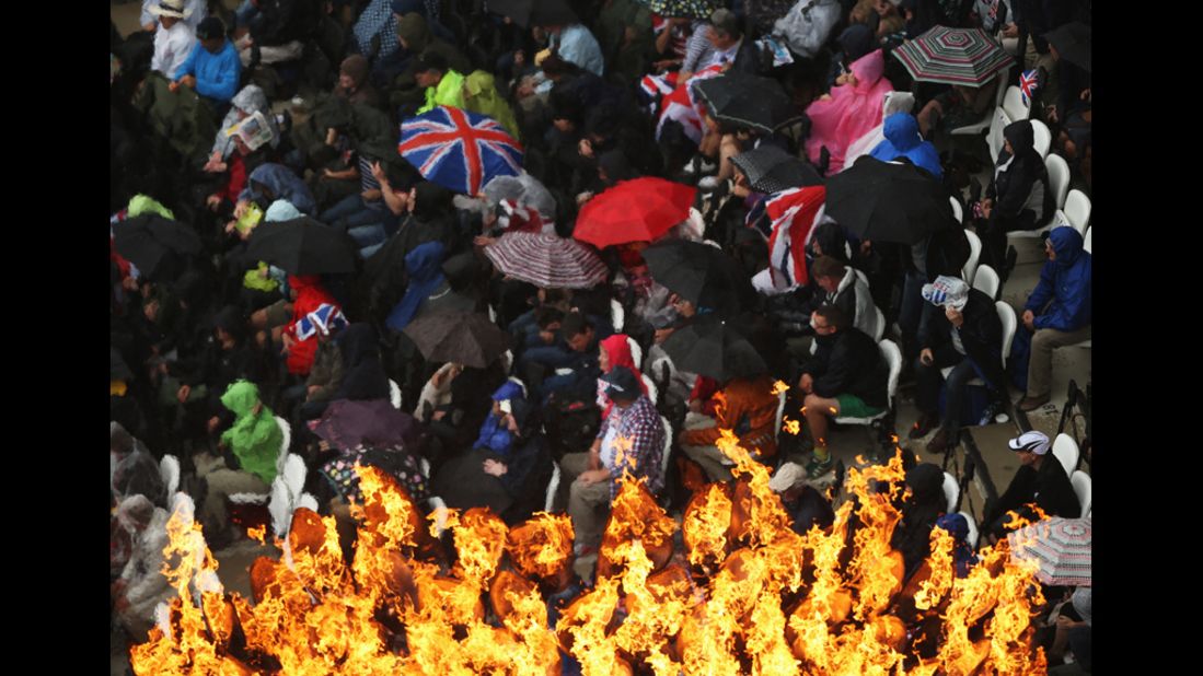 Fans take shelter from the rain, while the Olympic Cauldron remains aflame at Olympic Stadium.