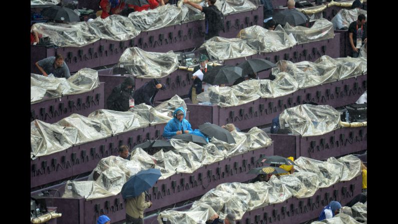 Journalists try to keep their equipment dry with rain covers at the Olympic Stadium.