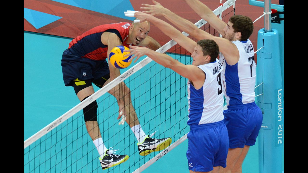 William Priddy, left, spikes as Russia's Nikolay Apalikov, center, and Maxim Mikhaylov, right, attempt to block during a men's preliminary pool B volleyball match.
