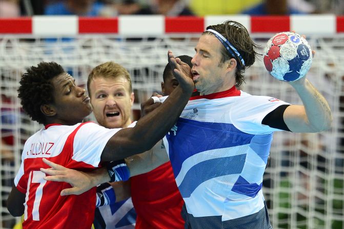 Britain's rightback Steven Larsson, right, tries to take a shot as Tunisia's leftback Wael Jallouz blocks during the men's preliminary Group A handball match.