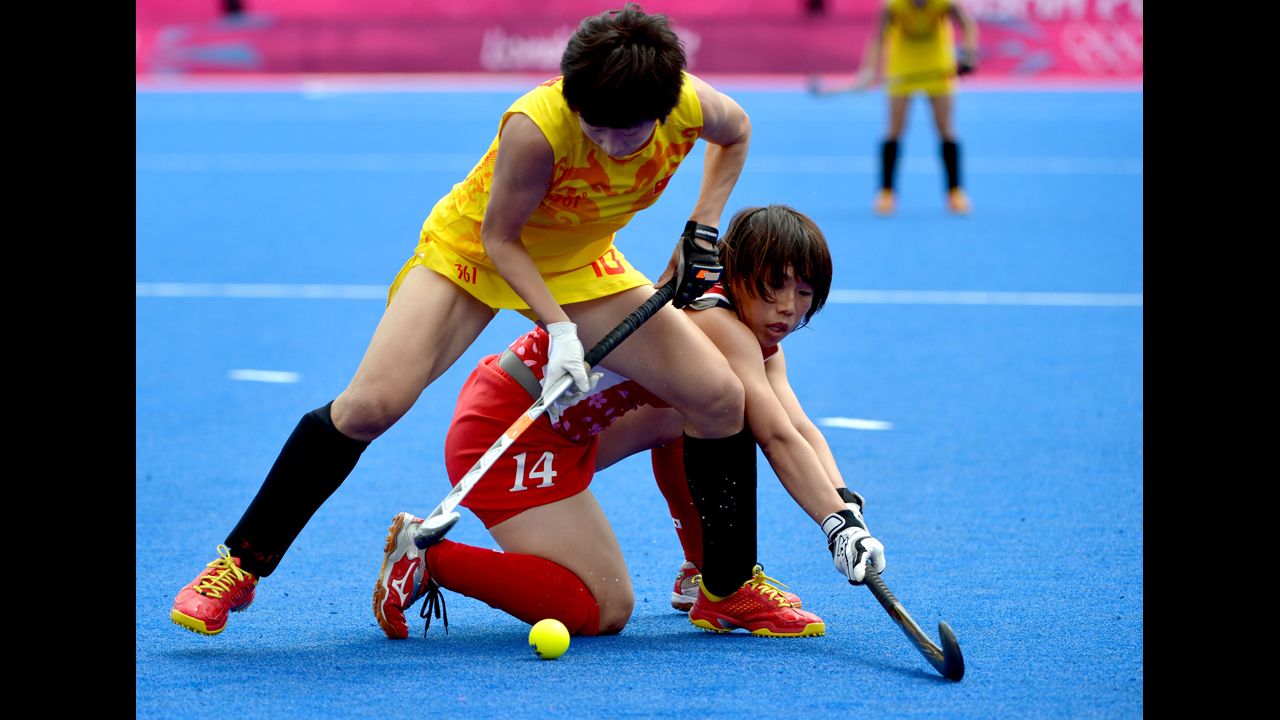 Gao Lihua of China, in yellow, is tackled by Manabe Kieko of Japan during the women's field hockey preliminary round match.