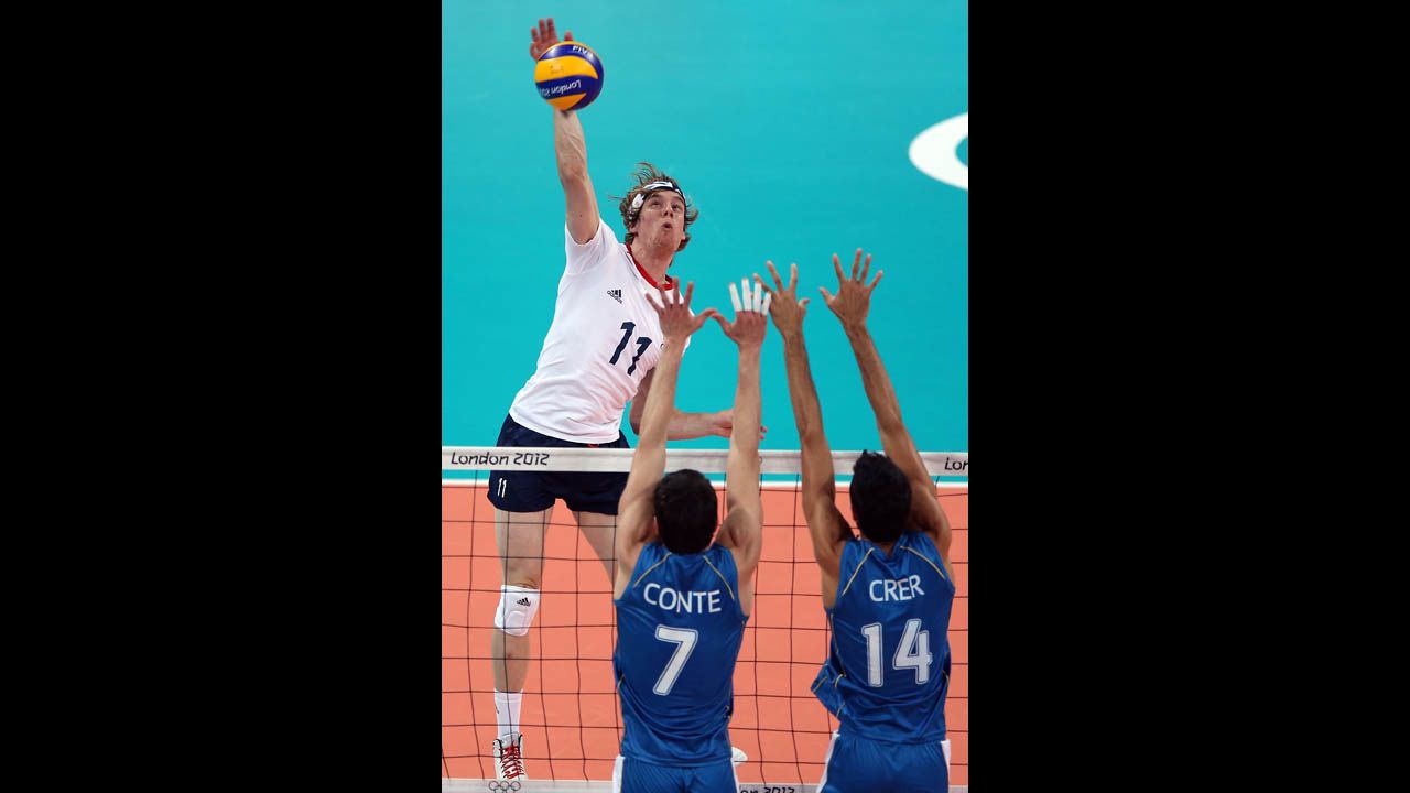 Joel Miller of Great Britain spikes the ball as Facundo Conte and Pablo Crer of Argentina defend during men's preliminary round Group A volleyball.