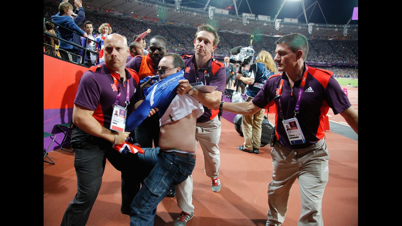 A spectator is detained by security after a beer bottle was thrown onto the track during the start of the men's 100-meter final.