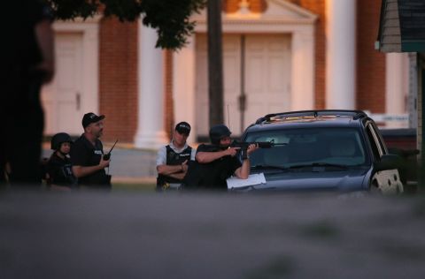 Officers take cover behind a vehicle as they secure the neighborhood where the shooter is believed to have lived in Cudahy, Wisconsin.