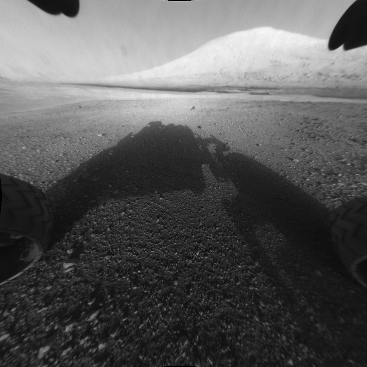 This image shows Curiosity's main science target, "Mount Sharp." The rover's shadow can be seen in the foreground. The dark bands in the distances are dunes. 