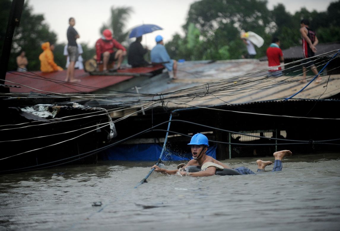 A man tries to cross floodwaters by following a rope as other residents wait on their roofs in Manila.