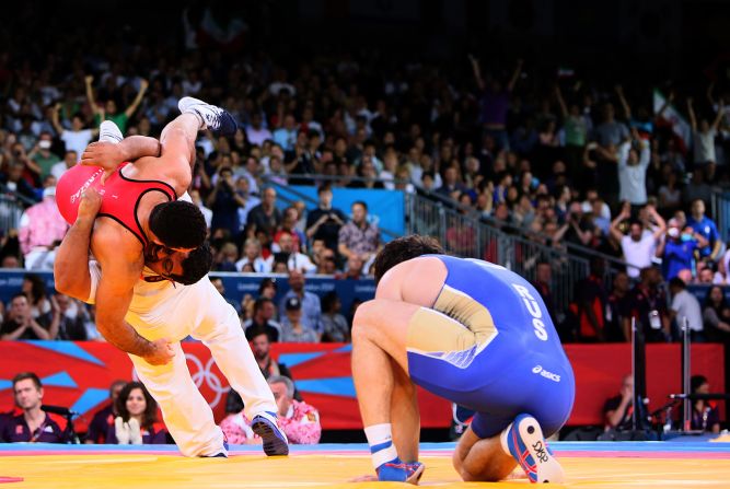 Iran's Ghasem Gholamreza Rezaei, left, celebrates with his coach, center, after defeating Russia's Rustam Totrov, right, in their 96 kilogram Greco Roman wrestling final fight.
