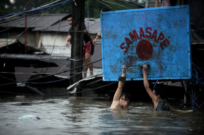Two men hang onto a basketball hoop in deep floodwaters in Manila.
