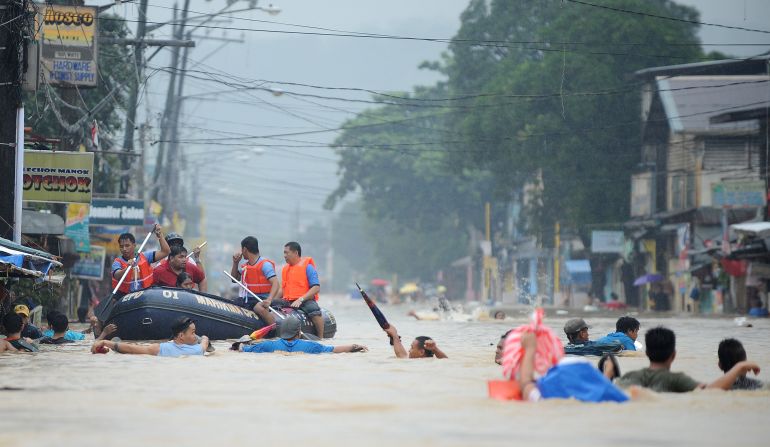 Residents wait on the roofs of buildings as rescuers make their way down a flooded street in Tumana.