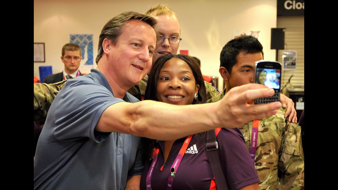 British Prime Minister David Cameron, left, takes a photo with Olympic volunteer Anita Akuwudike as he meets some of the volunteer work force at the ExCeL center in London.