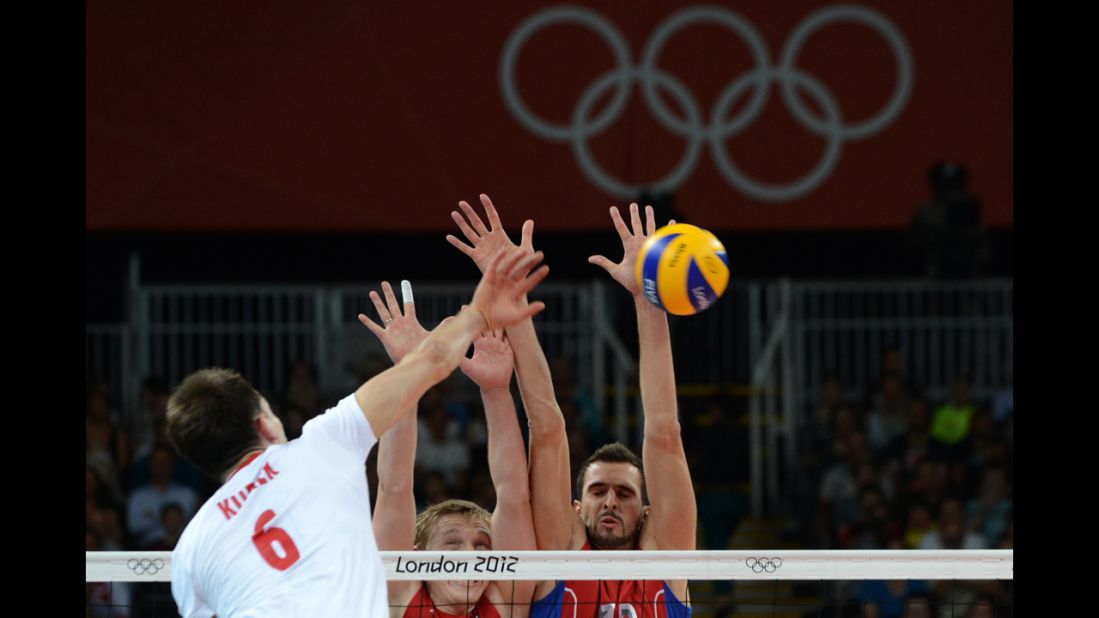 Poland's Bartosz Kurek, left, spikes as Russia's Sergey Grankin, center, and Alexander Volkov attempt to block during the men's quarterfinal volleyball match.