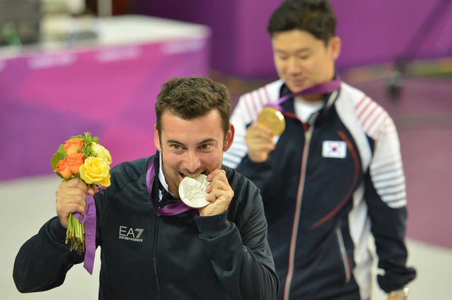 Italy's Luca Tesconi bites his silver medal as gold medalist South Korea's Jin Jong-oh stands behind him. They competed in the 10-meter air rifle men's final. 