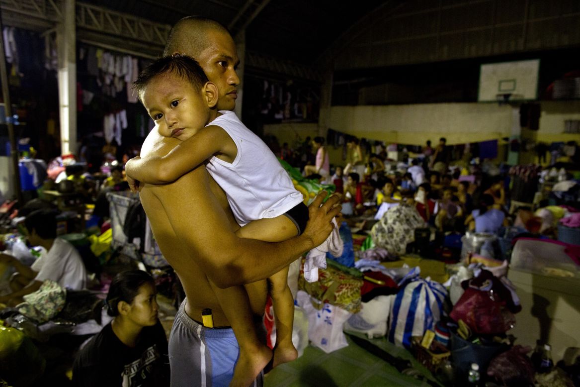 A flood victim holds his son at a crowded evacuation center in Manila.