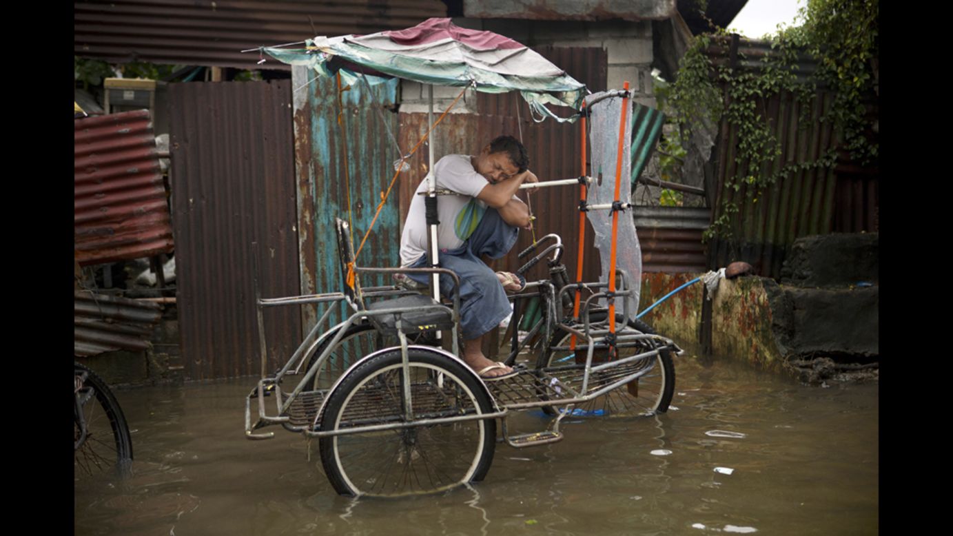 A pedicab driver sleeps on his vehicle along a flooded street in Manila.