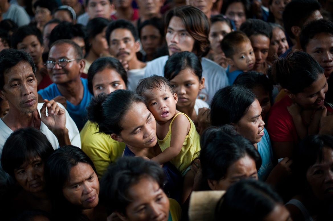 A woman holds a crying baby as she and thousands of flood victims line up for food relief at a municipal building in Paombong.