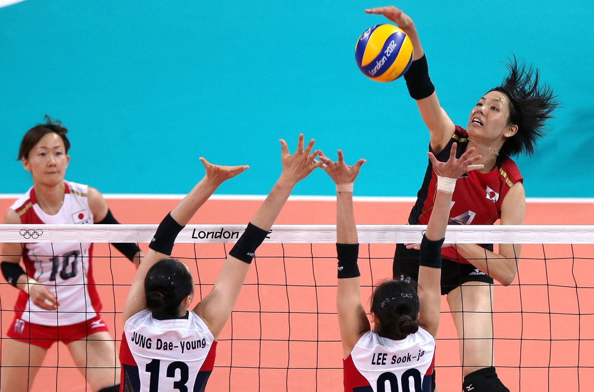 No. 14 Saori Sakoda of Japan spikes the ball against No. 13 Dae-Young Jung and No. 20 Sook-Ja Lee of South Korea during a women's volleyball match.