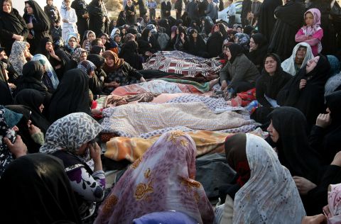 Bodies recovered from the rubble lie covered as villagers mourn their deaths.