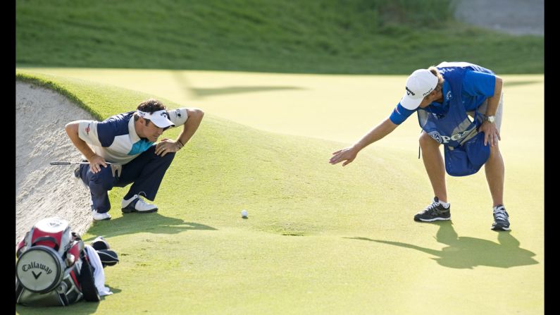 Trevor Immelman of South Africa and his caddy examine the green before a putt.