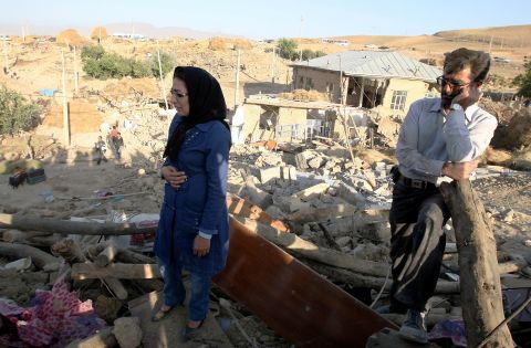 An Iranian man and woman stand on top of the rubble of their destroyed house in the village of Baje-Baj on Sunday.