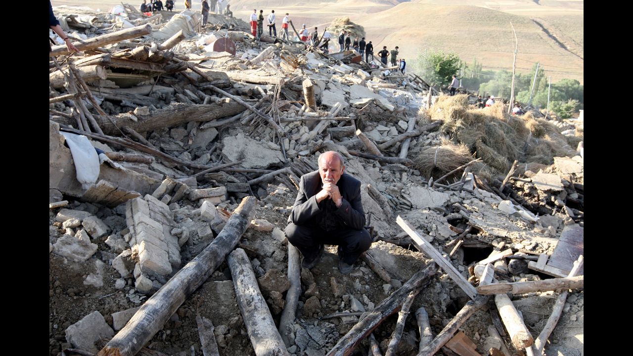 An Iranian resident from the village of Baje-Baj, near the town of Varzaqan, stands on top of the rubble of his destroyed home.