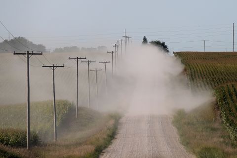 A car kicks up dust as it drives by corn fields on dry dirt road in State Center, Iowa.