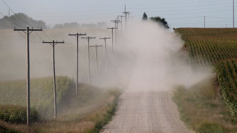A car kicks up dust as it drives by corn fields on dry dirt road in State Center, Iowa.