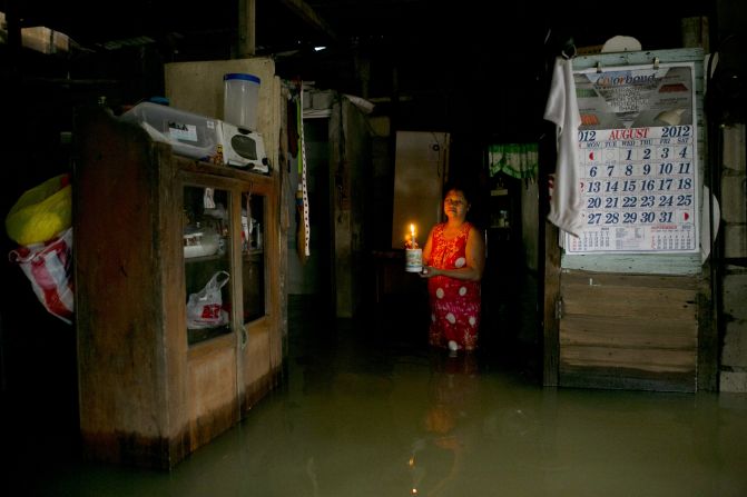 A woman lights her flooded home with a candle in Bulacan.