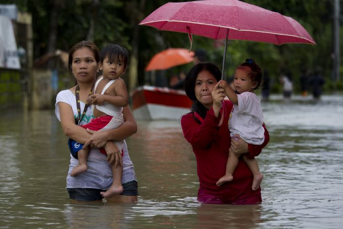 Mothers carry their children through a flooded street.