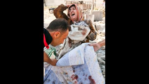 A Syrian woman holds her dead baby as she screams upon seeing her husband's body being covered following an airstrike by regime forces on the town of Azaz on August 15, 2012.